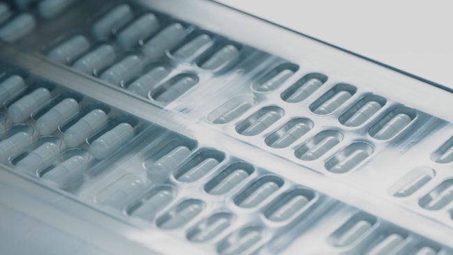 Blister packs with medicinal capsules move along the conveyor. Stage of fabrication. Plastic package with capsule meds. Medication capsules in blisters. Pharmaceutical factory production line